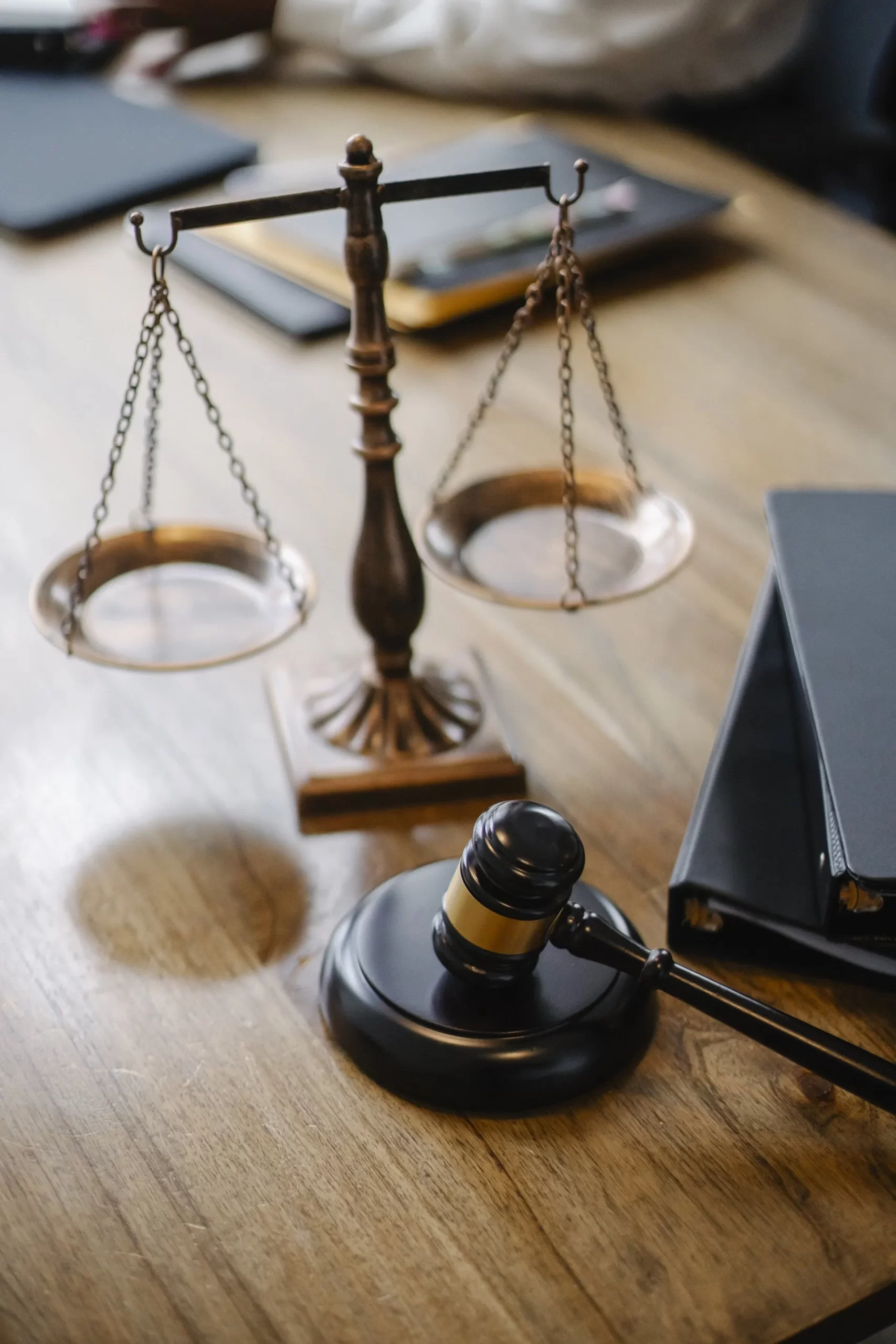 Scales of justice and a gavel on a wooden table, symbolizing law and legal proceedings, with black folders nearby.